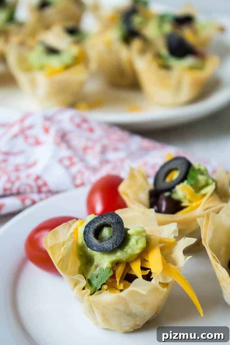 Irresistible Game Day Appetizer Recipes 7 Mini tacos filled with cheese, guacamole and topped with a sliced black olive.