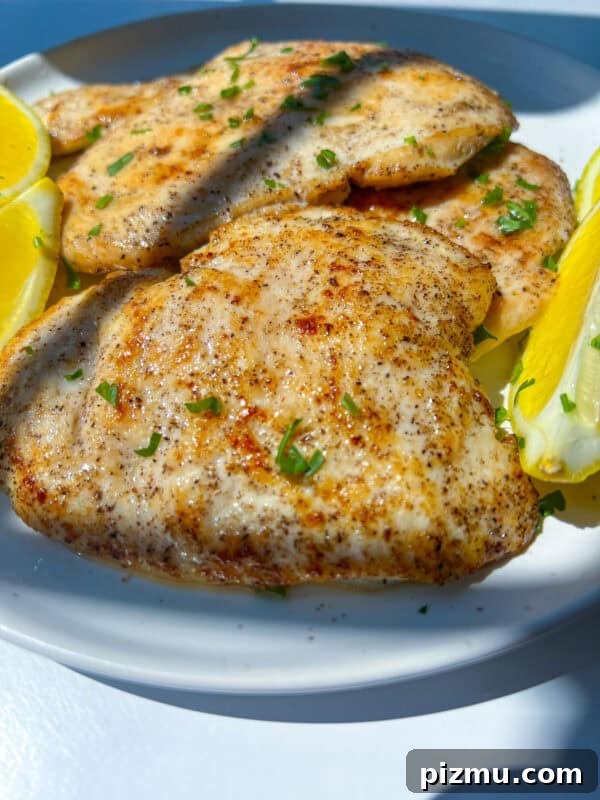 Juicy Grilled Lemon Chicken with Garlic and Herbs 9 Grilled Lemon Chicken breasts garnished with chopped herbs, served on a white plate with lemon wedges on the side.