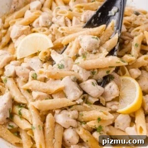 One-Pan Chicken Piccata Pasta with Lemon and Capers 18 Penne chicken piccata pasta with diced chicken, lemon wedges, and herbs, mixed in a creamy sauce, served in a white dish with a black serving spoon.