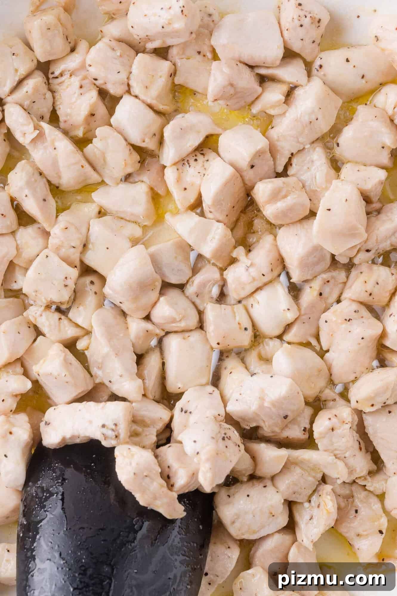 One-Pan Chicken Piccata Pasta with Lemon and Capers 4 Cubed pieces of chicken breast are being cooked in a pan, with a black spatula stirring the lightly browned and seasoned meat.