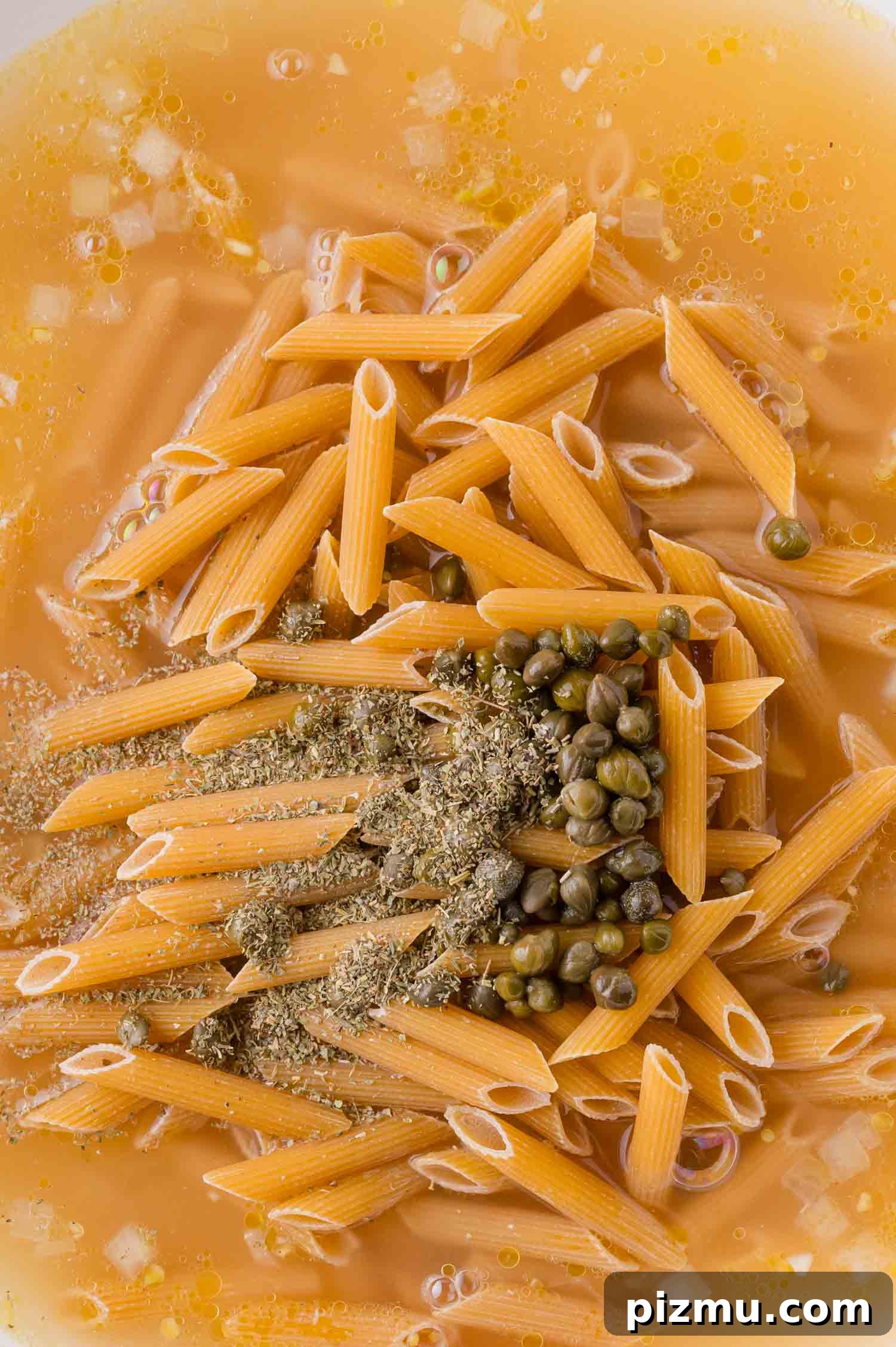 One-Pan Chicken Piccata Pasta with Lemon and Capers 7 Uncooked penne pasta, capers, herbs, and spices in a broth or liquid, prepared for cooking.