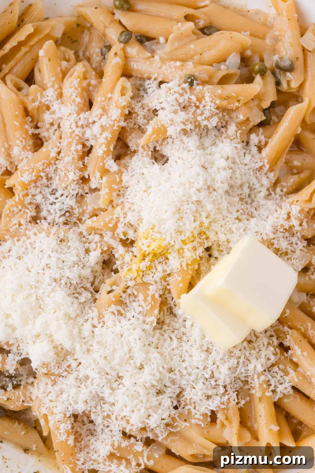 One-Pan Chicken Piccata Pasta with Lemon and Capers 10 Close-up of cooked penne pasta topped with grated cheese and a pat of butter.