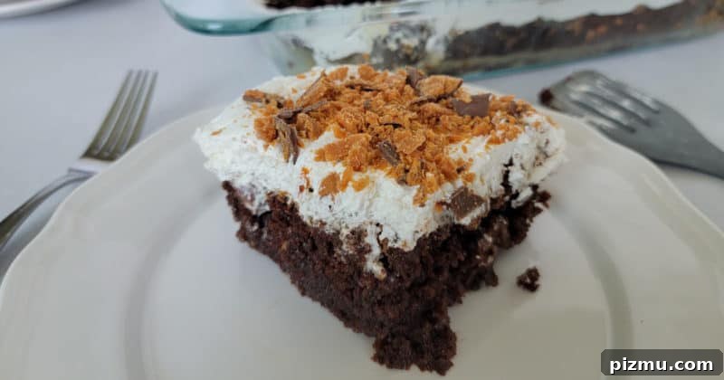 Butterfinger Cake Recipe with Chocolate Peanut Butter Crunch 10 square of Butterfinger poke cake on a white plate next to forks