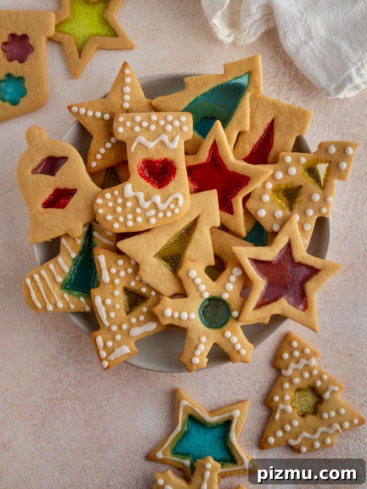 20 Classic Christmas Cookie Recipes to Bake This Season 11 stained glass window cookies stacked on plate on pink background.