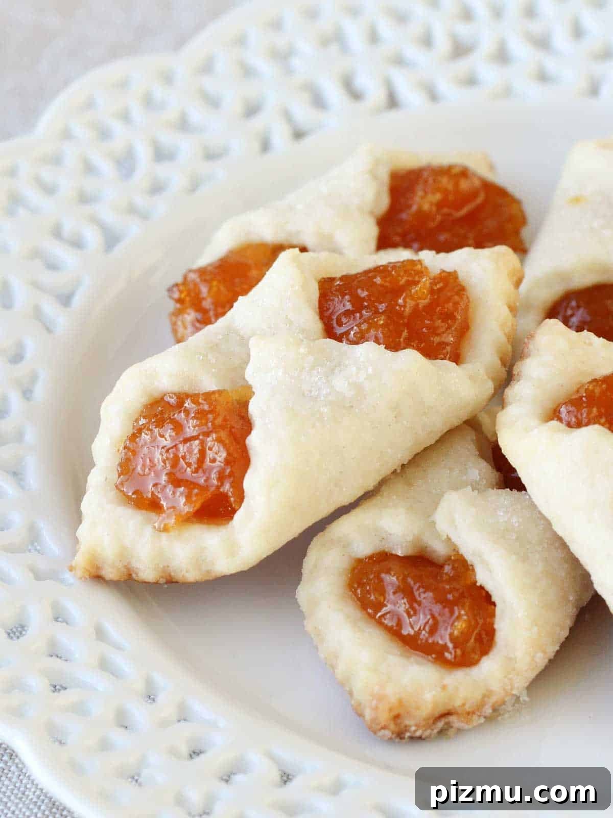 20 Classic Christmas Cookie Recipes to Bake This Season 17 apricot kolacky cookies stacked on white lace plate.
