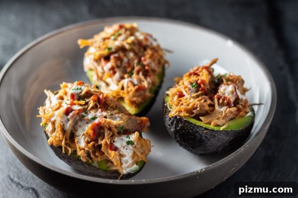 Stuffed avocados or avocado boats with pulled pork, cheese, and BBQ sauce in a bowl.