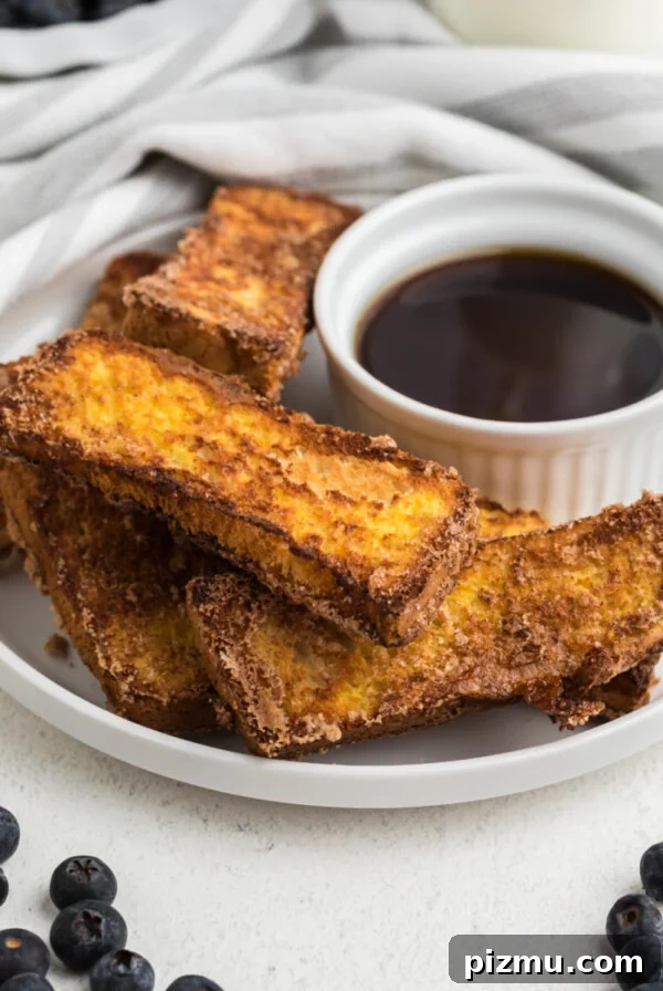 French toast sticks made in the air fryer on a white plate with blueberries surrounding it.