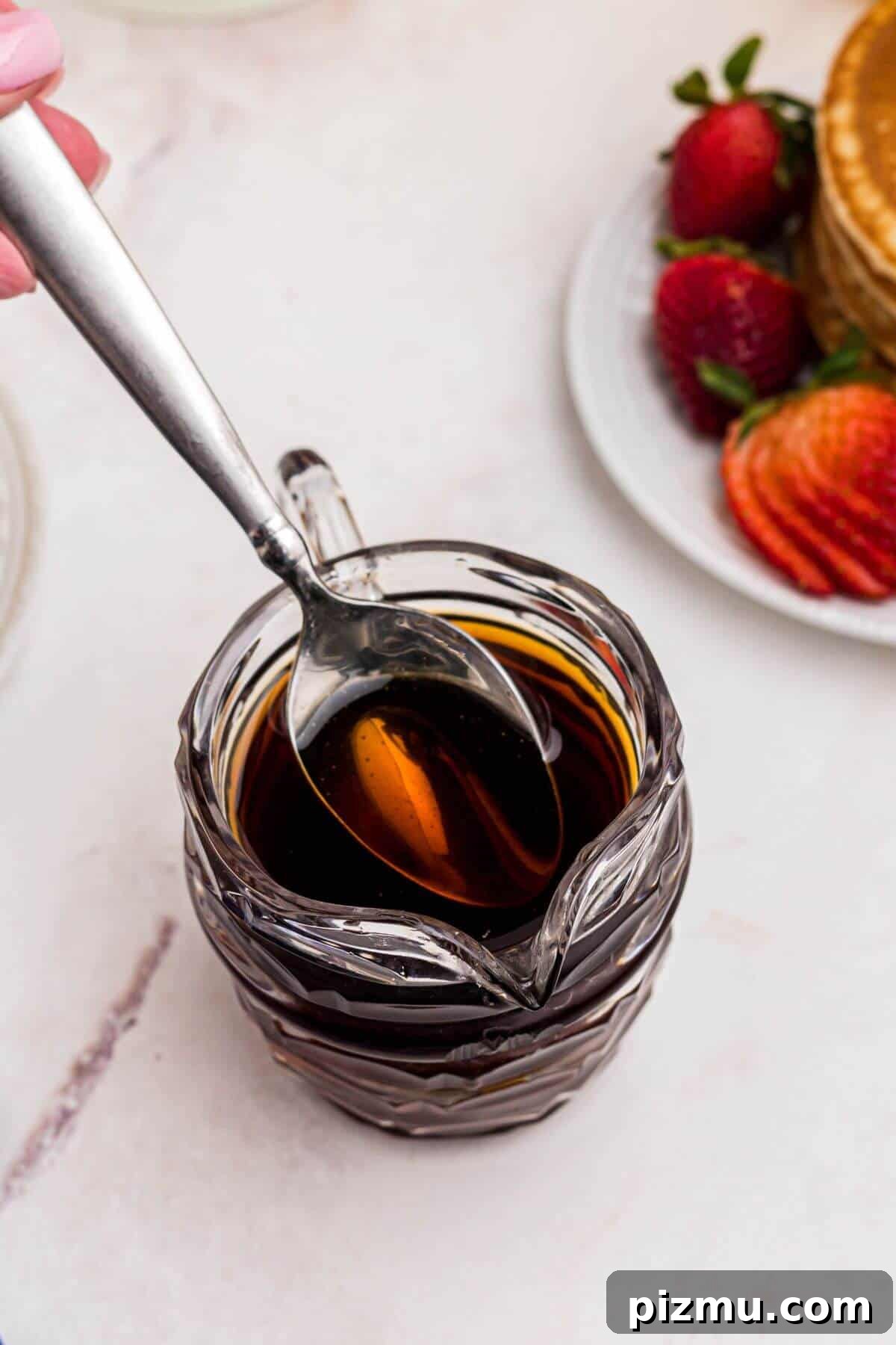 Freshly homemade syrup in a clear glass serving dish with a spoon lifting some syrup out.