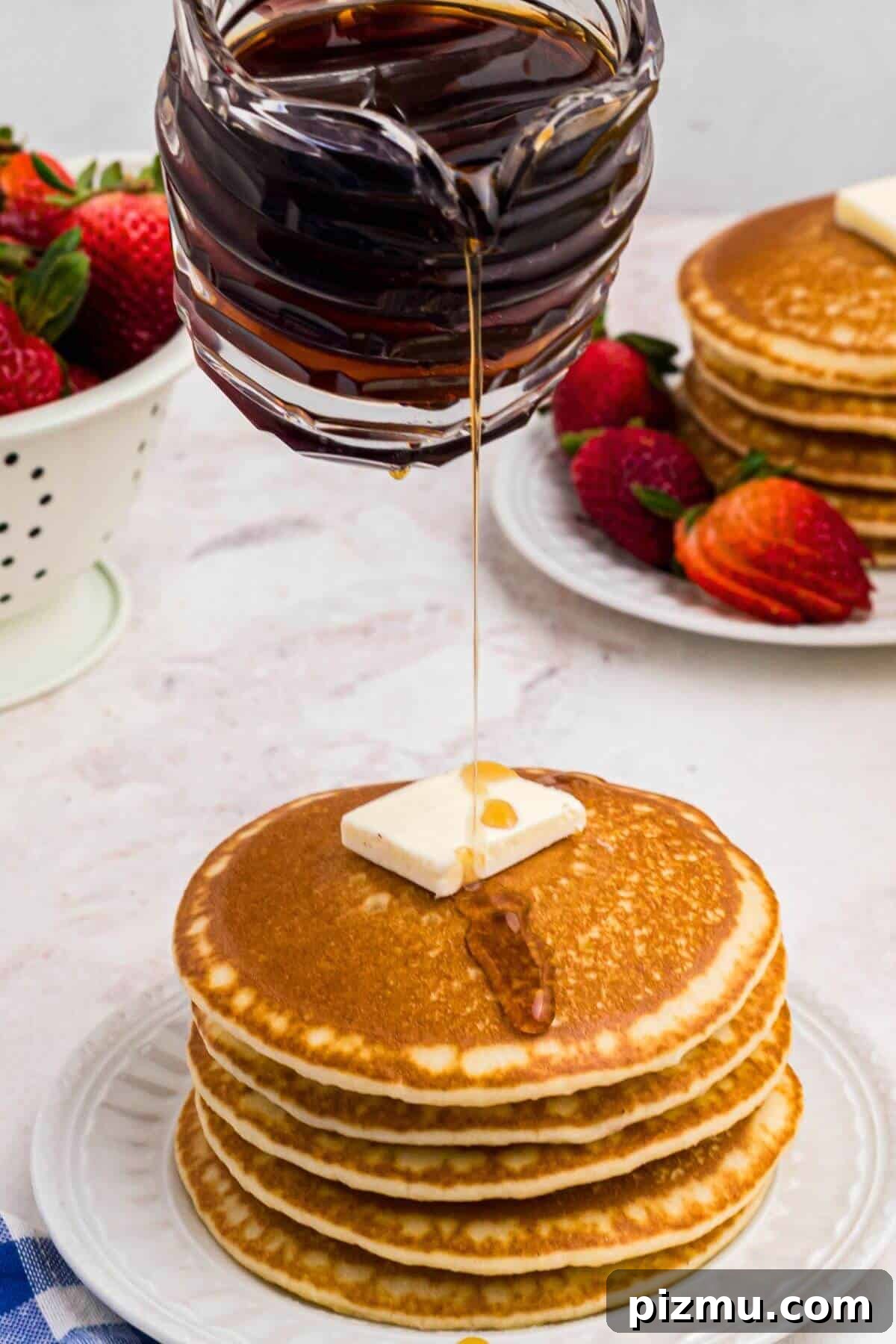 Syrup being poured over a stack of pancakes.