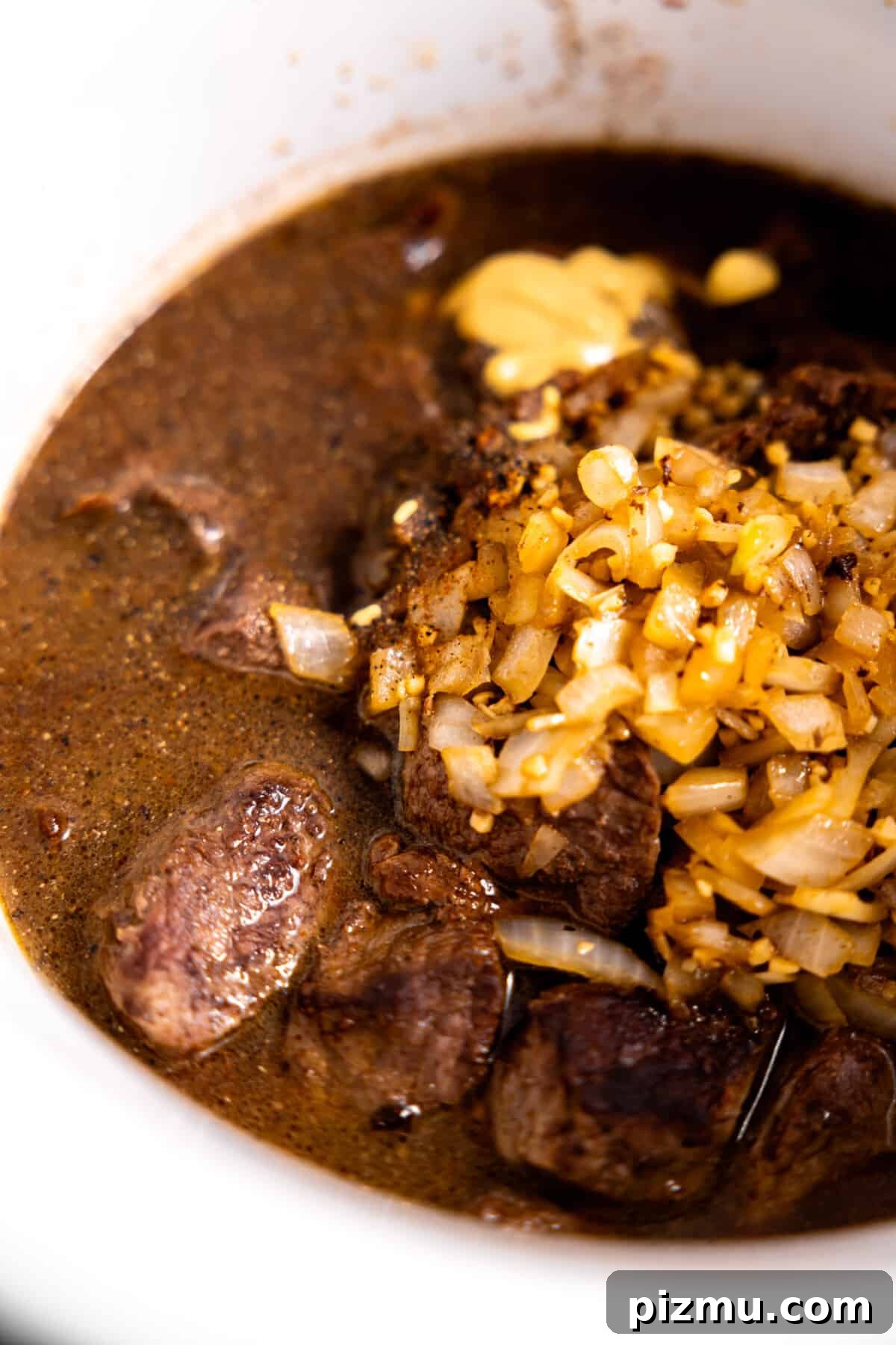 Seared beef in broth with onions and garlic added to slow cooker.