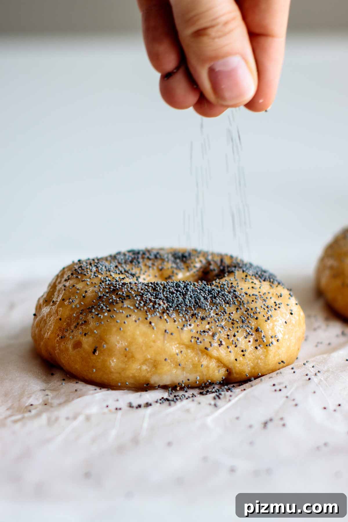 How to Make Sourdough Bagels at Home 7 hand topping boiled bagel with poppy seeds
