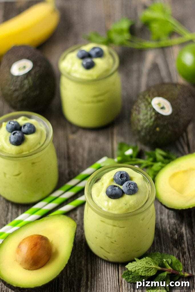 Creamy Tropical Avocado Smoothie Recipe 3 side shot of tropical avocado smoothies on wooden surface with fresh avocados in perimeter of shot