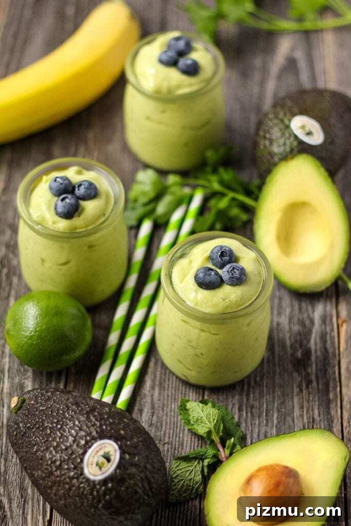 Creamy Tropical Avocado Smoothie Recipe 5 side shot of tropical avocado smoothies in clear glasses on wooden surface topped with fresh blueberries.