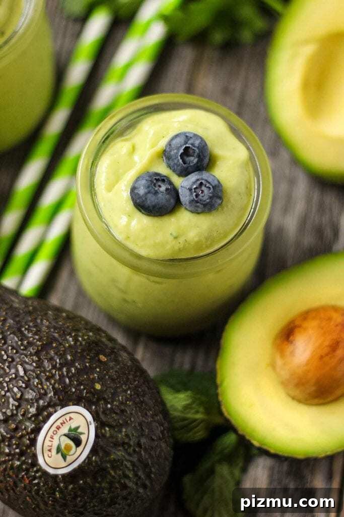 Creamy Tropical Avocado Smoothie Recipe 7 close up of tropical avocado smoothie in clear glass with fresh avocados in perimeter.