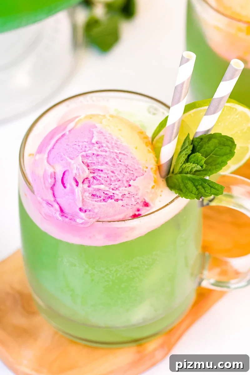 Close up photo of a mug filling with green punch topped with rainbow sherbet and garnished with lime slice and mint.
