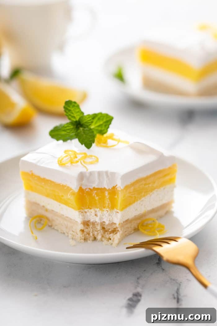 Creamy Layered Lemon Trifle Recipe 2 Bite taken from the corner of a slice of layered lemon dessert on a white plate.