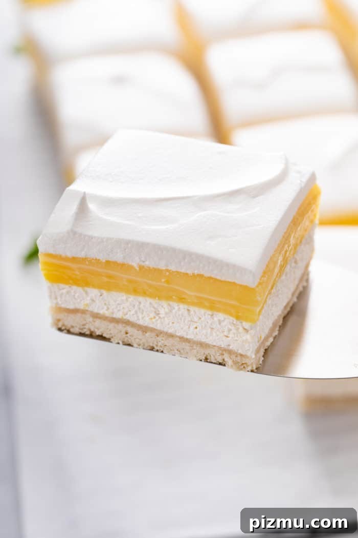 Creamy Layered Lemon Trifle Recipe 11 Cake server holding up a slice of layered lemon dessert, with more slices visible in the background.