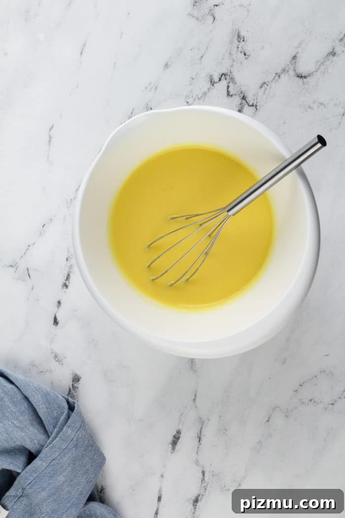 Creamy Layered Lemon Trifle Recipe 8 Lemon pudding being whisked together in a white mixing bowl for layered lemon dessert.