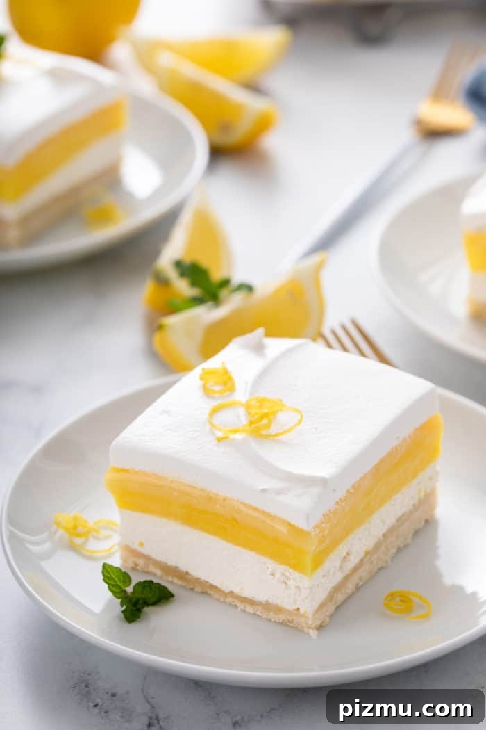 Creamy Layered Lemon Trifle Recipe 10 White plate holding a slice of layered lemon dessert that is garnished with lemon zest.