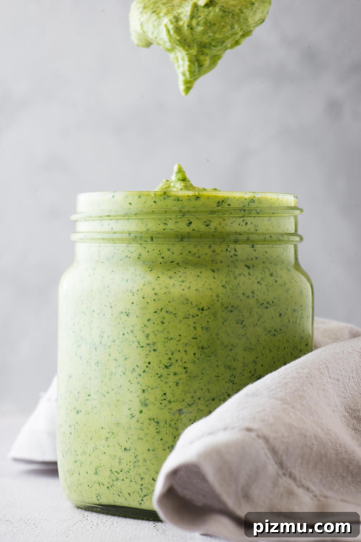 A mason jar filled to the brim with thick vegan green tahini sauce.