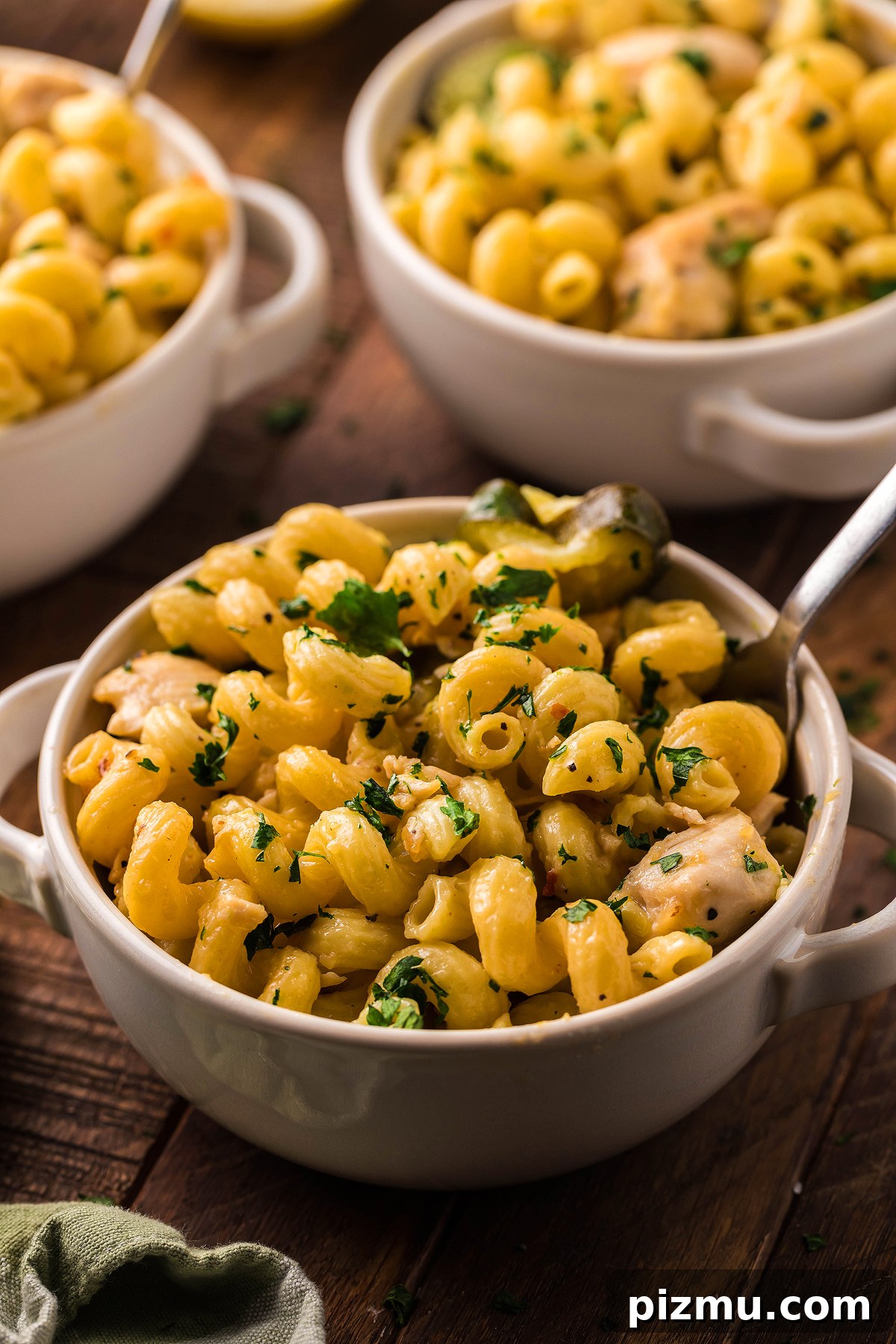 Creamy Lemon Chicken Pasta in the Instant Pot 11 Three bowls of creamy pasta with chicken and vegetables, garnished with fresh herbs, are served on a wooden table with spoons.
