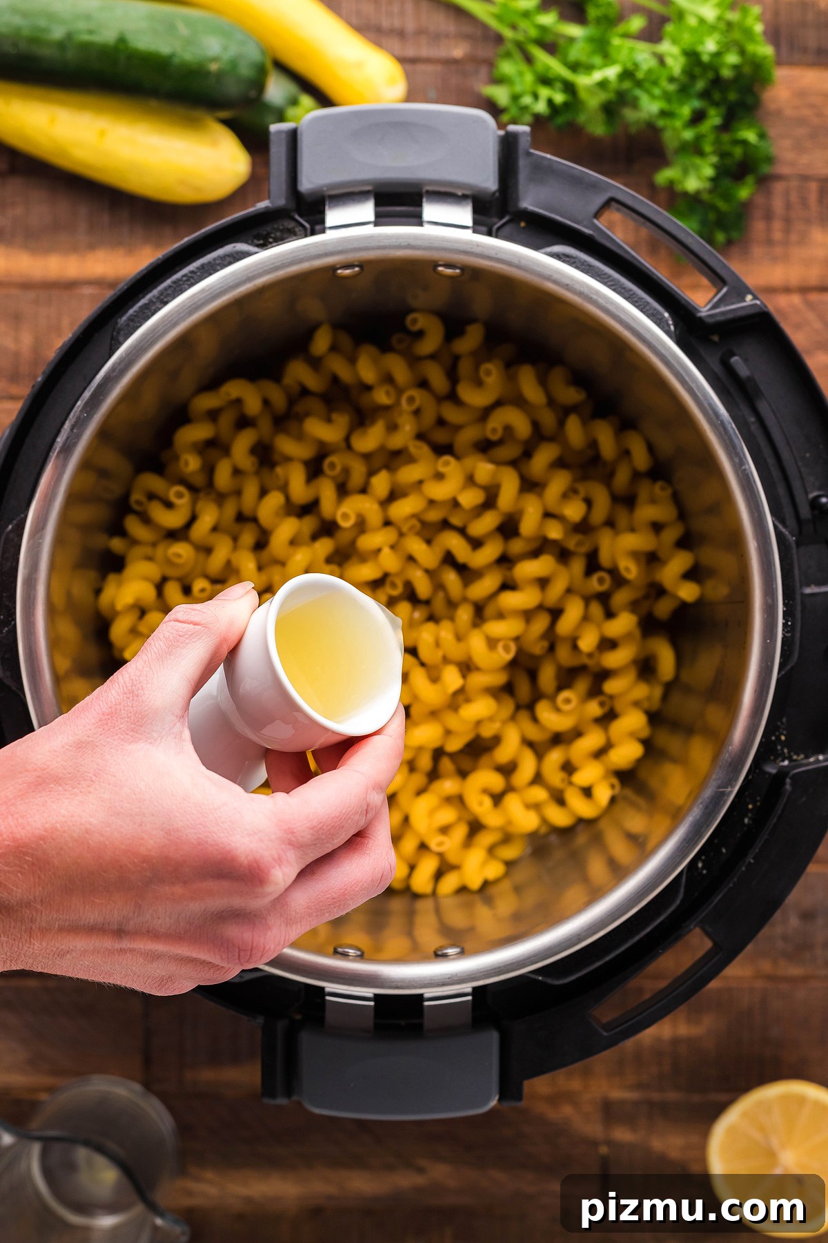 Creamy Lemon Chicken Pasta in the Instant Pot 14 A hand pours liquid from a small cup into an Instant Pot filled with dry elbow macaroni, preparing an easy instant pot pasta dinner.