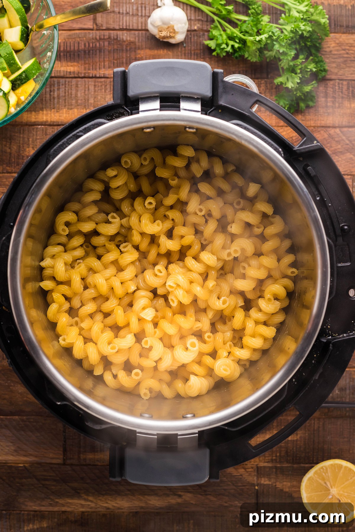 Creamy Lemon Chicken Pasta in the Instant Pot 16 Cavatappi pasta cooking in an Instant Pot for a delicious instant pot pasta dinner, surrounded by lemon, parsley, garlic, and vegetables on a wooden table.