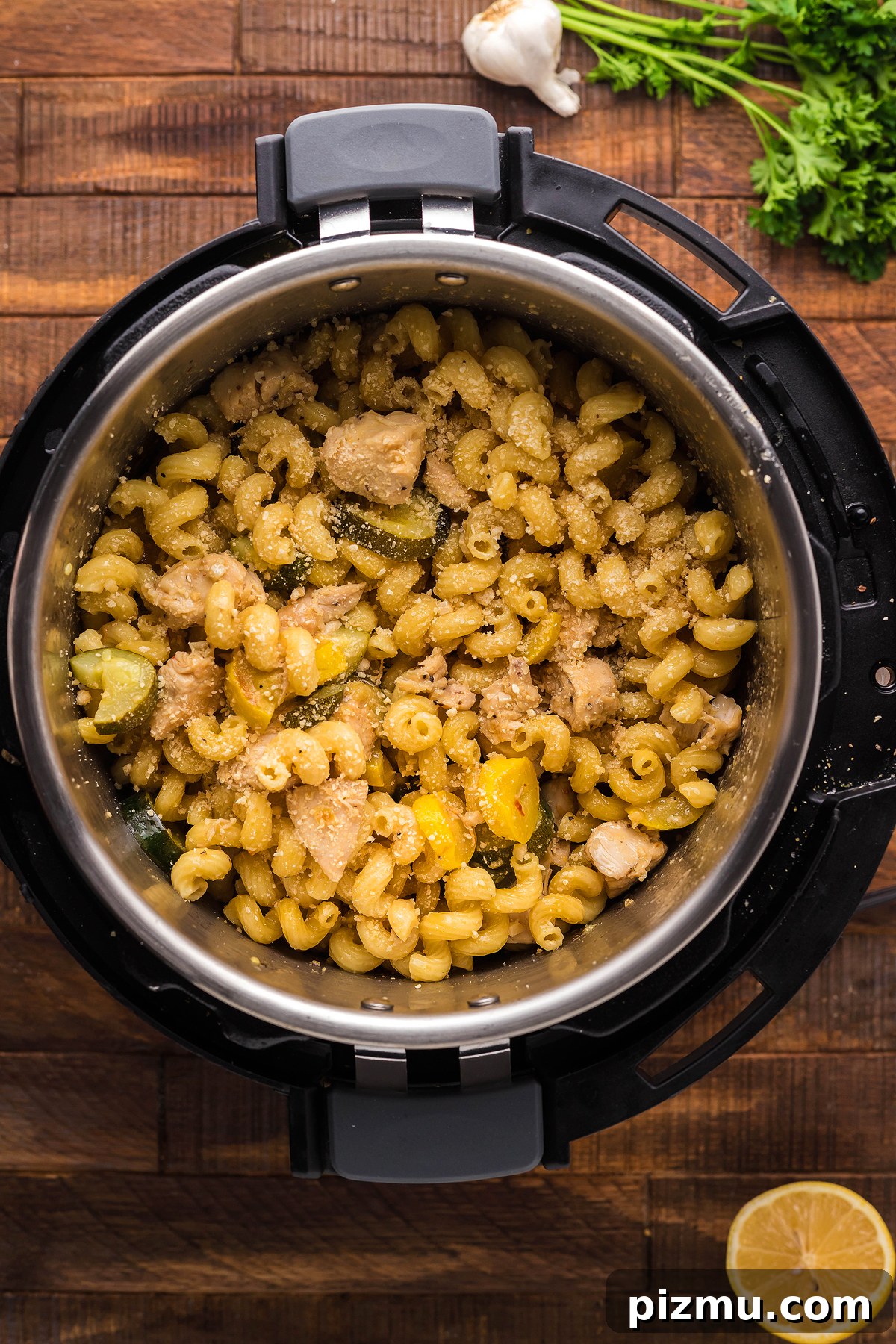 Creamy Lemon Chicken Pasta in the Instant Pot 18 Instant Pot Lemon Chicken Pasta features cooked pasta with chicken and vegetables, served on a wooden surface alongside fresh herbs, garlic, and lemon for a bright instant pot pasta dinner.