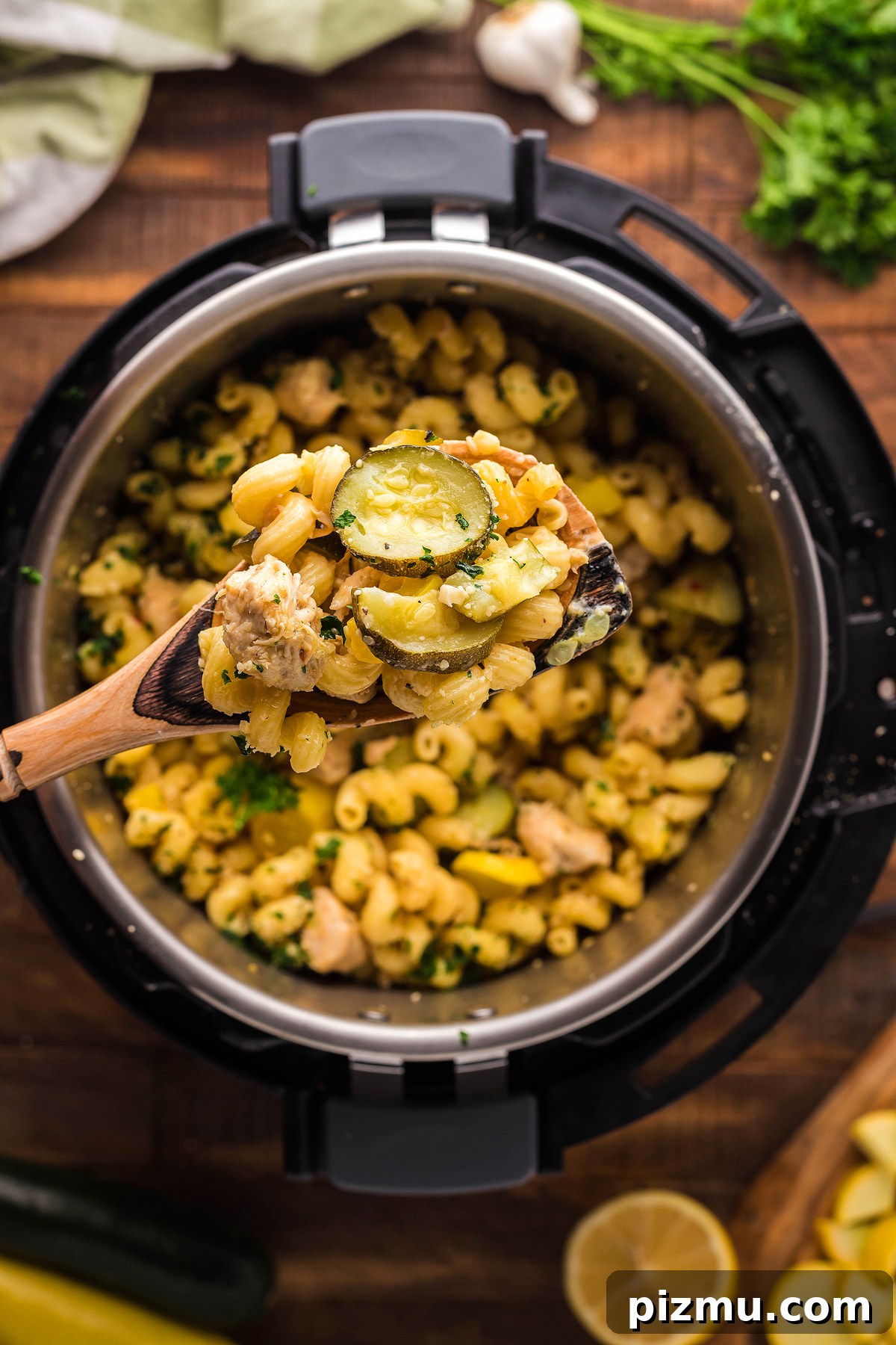 Creamy Lemon Chicken Pasta in the Instant Pot 9 A wooden spoon holds cheesy pasta with chicken and vegetables, featuring zucchini, over a pot on a wooden table.