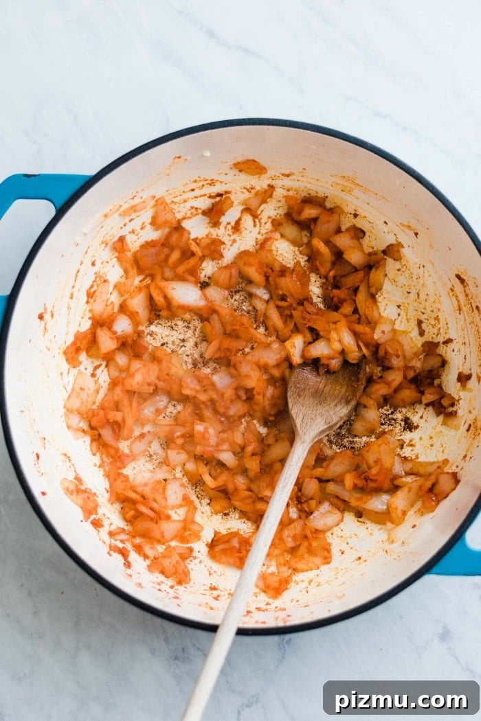 Creamy Red Curry Lentils with Coconut and Spinach 4 Diced onions cooking in red curry paste in a large saucepan with a wooden spoon.