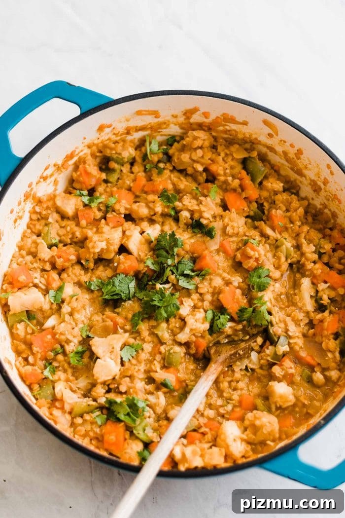 Creamy Red Curry Lentils with Coconut and Spinach 6 A red lentil curry dish with various vegetables cooking in a large pot with a wooden spoon.