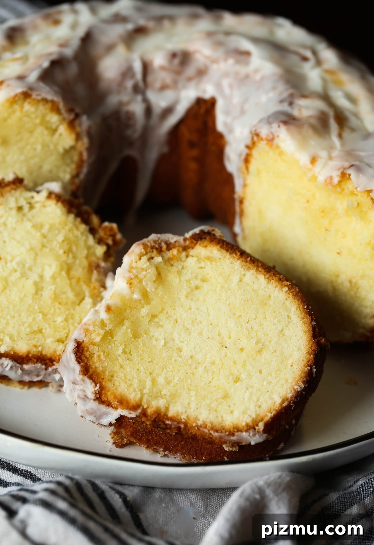 A deliciously simple, classic 7UP Cake tastes like a lemon pound cake with tons of old fashioned charm! This moist, tender cake is made from scratch in a bundt pan and drizzled with a homemade lemon glaze. Close up of cake slices next to a 7UP bundt cake on a plate.