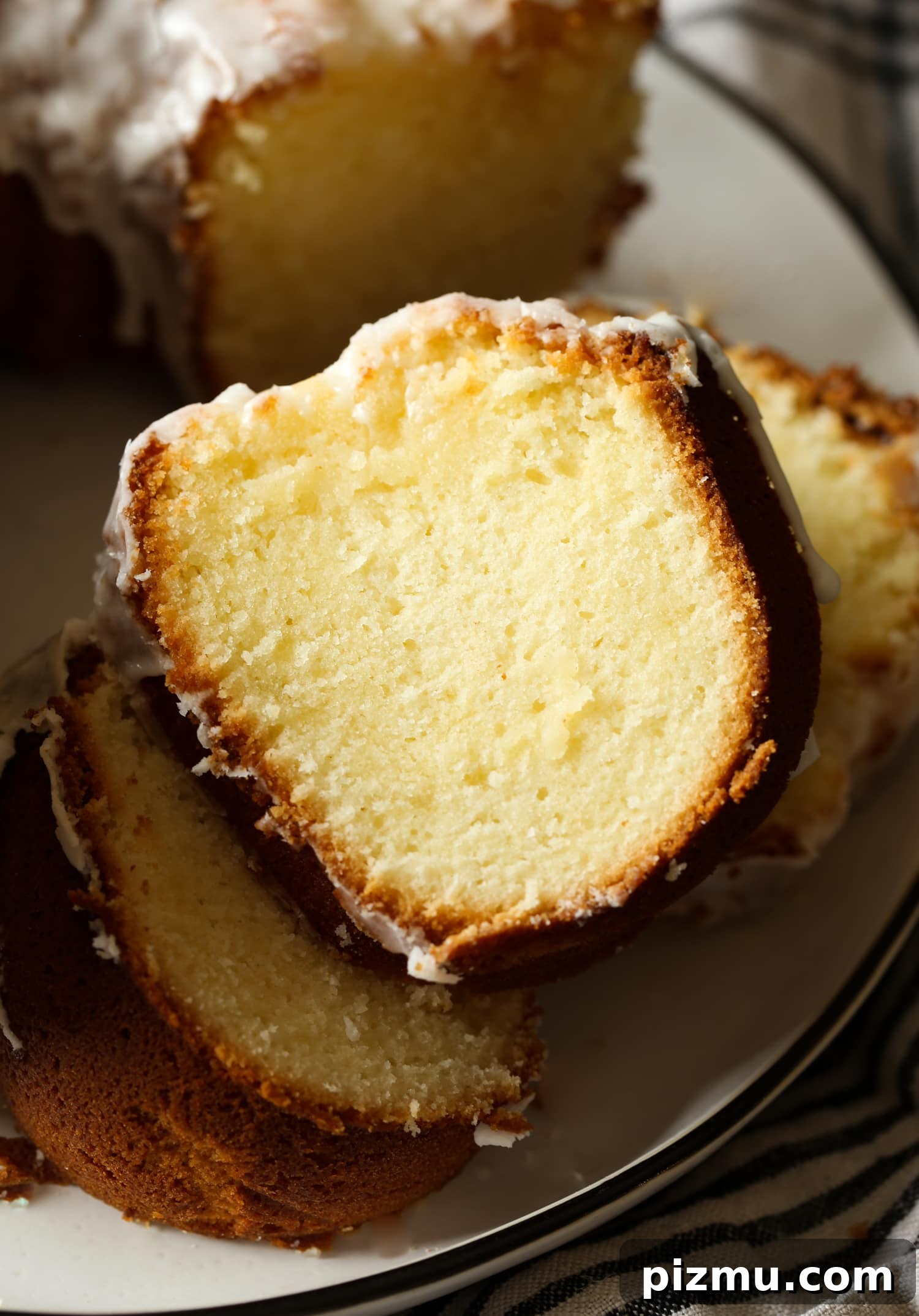 A deliciously simple 7UP Cake tastes like a lemon pound cake with tons of old fashioned charm! This moist, tender cake is made from scratch in a bundt pan and drizzled with a homemade lemon glaze. Close up of cake slices next to a 7UP bundt cake on a plate.