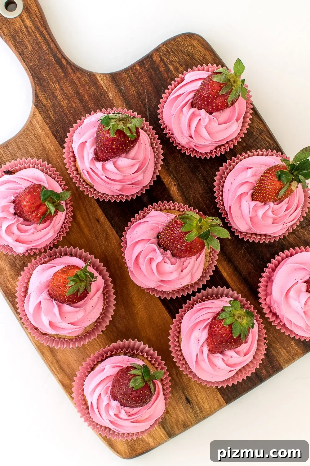 11 Keto Muffins for Quick Grab-and-Go Mornings 11 low carb and keto friendly Strawberry cupcake muffins with ruffled pink frosting and a fresh strawberry in pink paper wrappers.