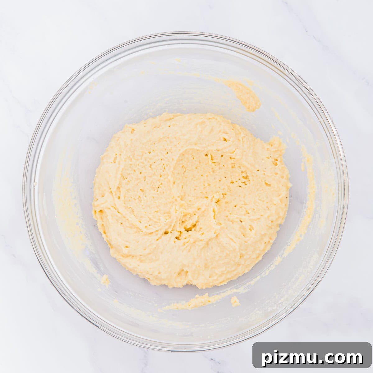 Flaky Almond Flour Biscuits Recipe 8 A glass mixing bowl filled with thick, creamy biscuit batter sits on a white marble surface.